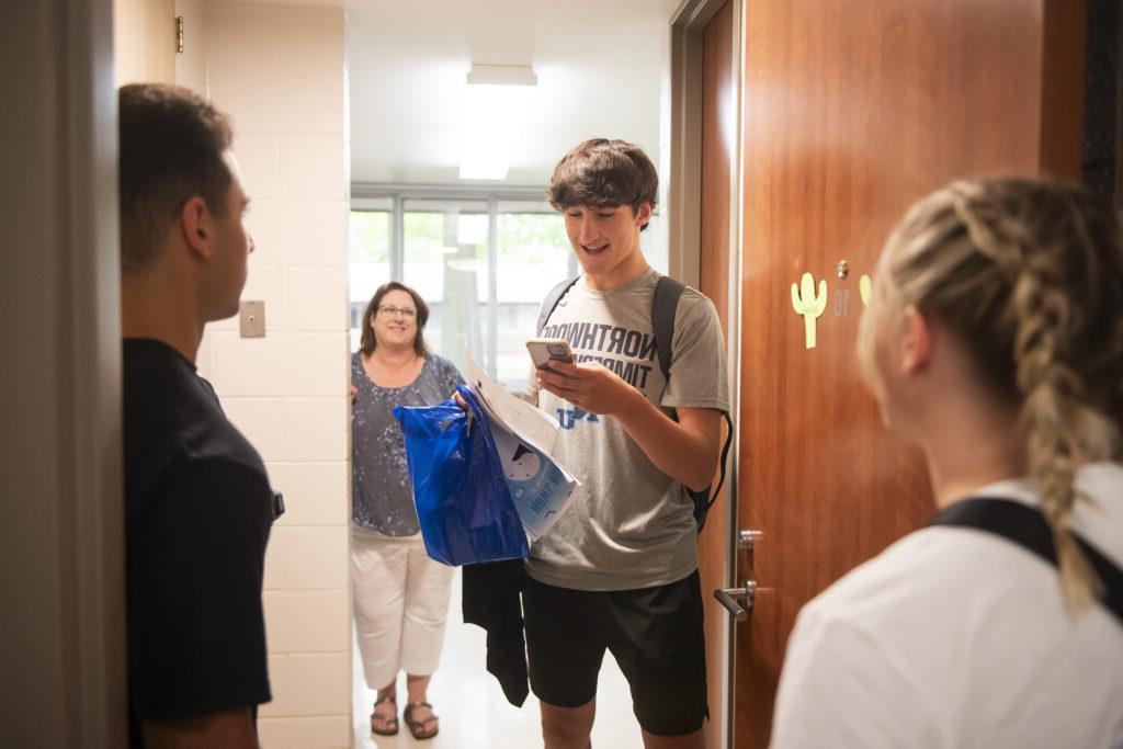 Northwood student smiling while looking at his phone in a dorm room